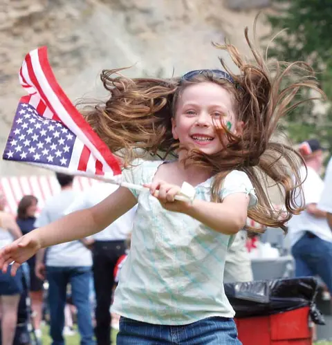 A young girl smiling and jumping while holding an American flag.