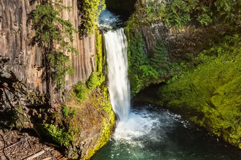 A waterfall flowing between rocky cliffs and green trees.
