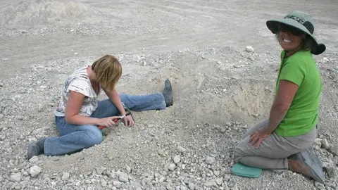 Two women search through gravel and rocks at a site.