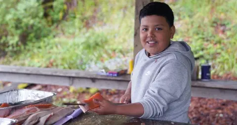A young person prepares fish outdoors.