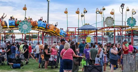 A crowd of people gathers near a roller coaster ride at a fair.