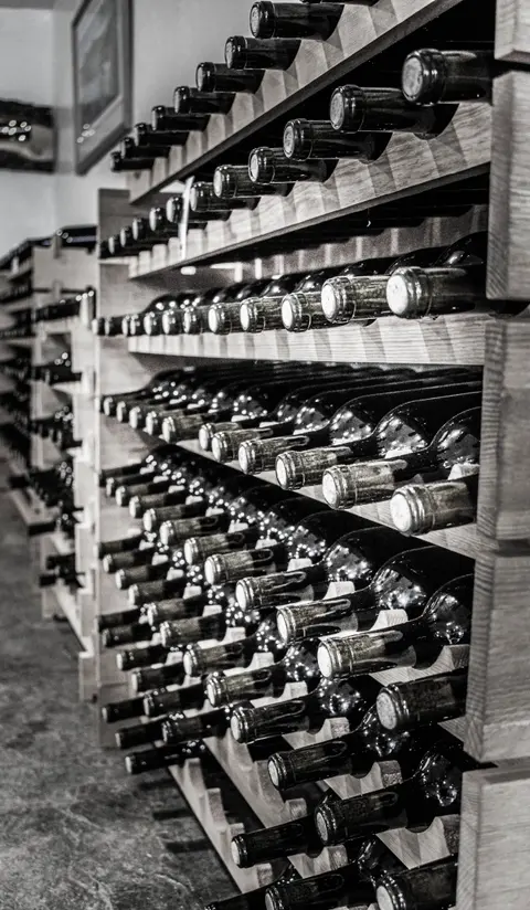 Black and white photograph showing multiple wooden racks filled with wine bottles in an interior space.