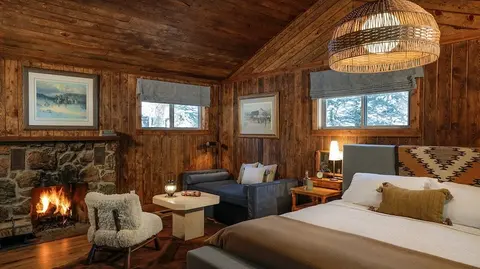 A cozy rustic bedroom featuring a stone fireplace and wood-paneled walls.