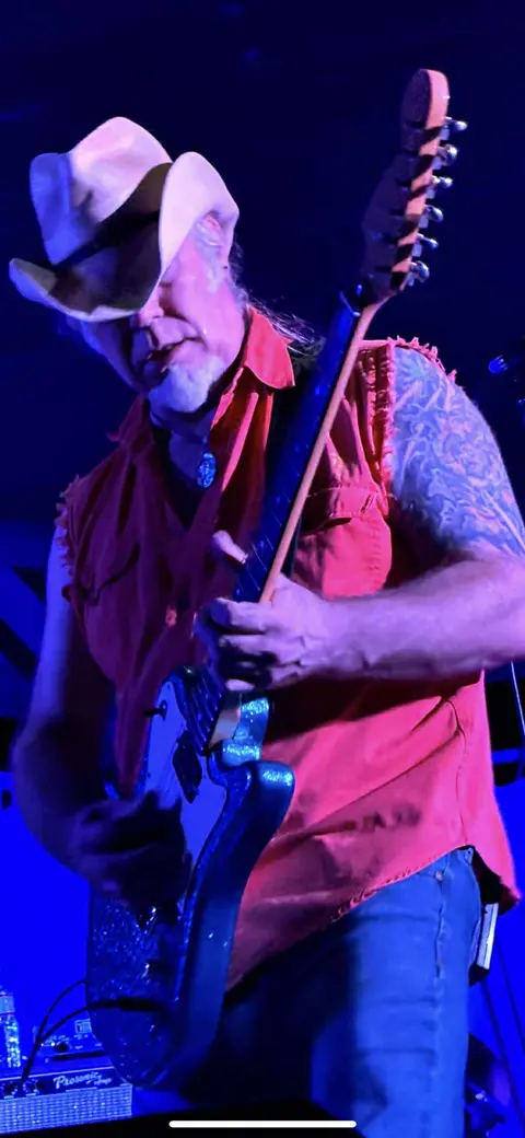 A musician wearing a cowboy hat plays an electric guitar on stage.