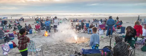 People gathered on a beach around a bonfire and fireworks.