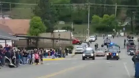 A procession of vehicles drives down a street lined with onlookers.