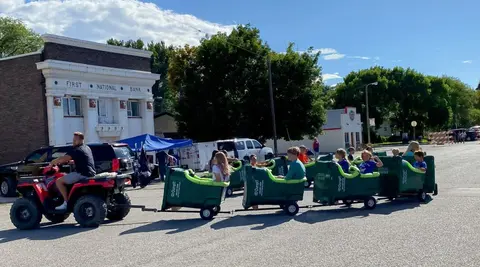 People ride in a makeshift train pulled by an ATV on a street.
