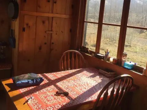 Interior view of a rustic room with a wooden table, chairs, and a window looking outside.