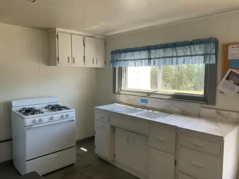 An interior view of a simple kitchen with white cabinets, a gas stove, and a window with a blue valance.
