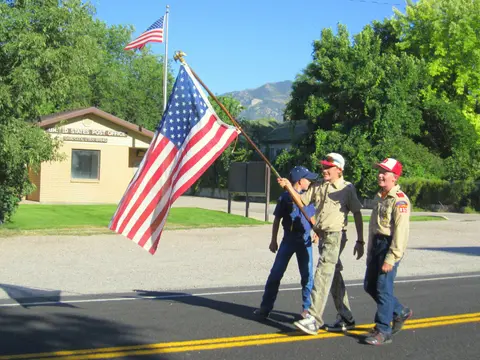 Three boys walk down a street carrying an American flag.