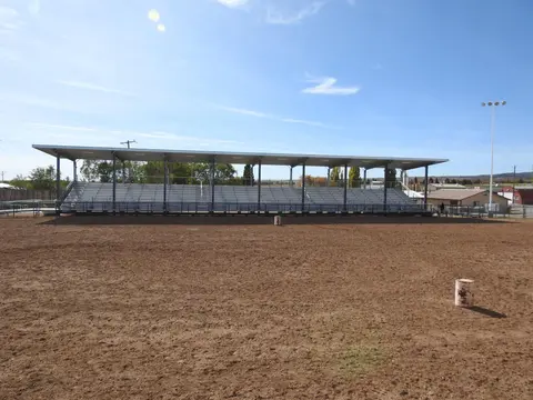 A covered grandstand overlooks a dirt arena under a blue sky.