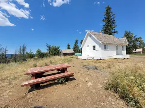 A white historic building stands on a hill with a red picnic table in the foreground.
