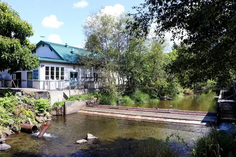 A building next to a river with a weir and trees.