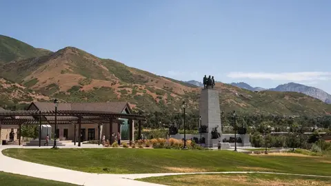 A monument stands in a park with mountains in the background.
