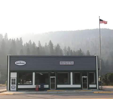 An exterior view of a building housing a post office and history center, with an American flag flying beside it.