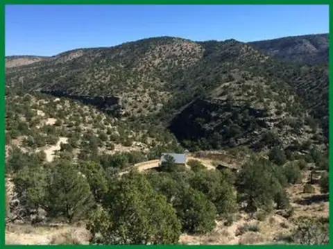 A landscape photograph showing a house nestled among hills and trees under a blue sky.
