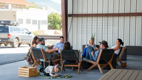 A group of adults sitting in chairs outdoors under a shelter while a child plays on the ground.