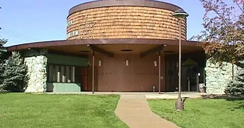 An exterior view of a modern round building with a stone and wood facade.