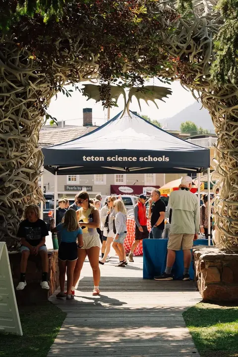 People walking through an antler archway near a tent for teton science schools.
