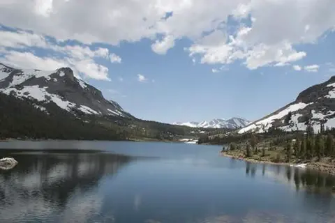 A scenic view of a calm alpine lake with snow-capped mountains in the background.