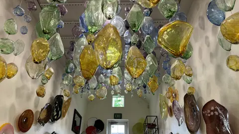 An indoor view of a ceiling installation made of hanging colorful glass art pieces.