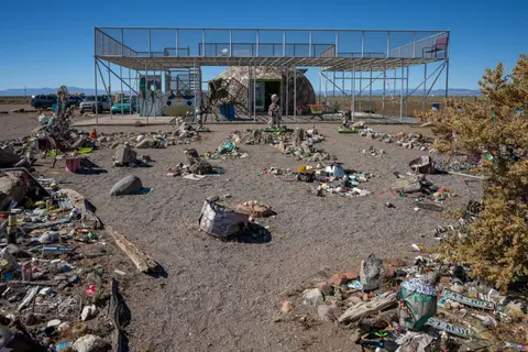 An outdoor view of a stone dome structure and metal frame building with miscellaneous items scattered around.