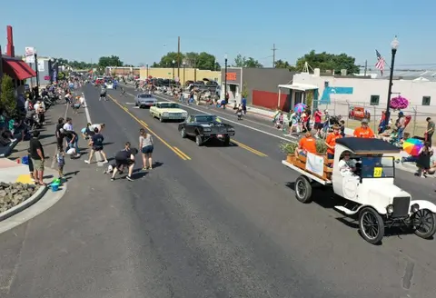 A street parade with vintage and classic cars and crowds watching.