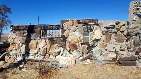 Exterior view of a ruined building constructed with stones and railroad ties under a clear blue sky.