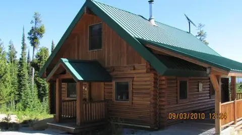 A wooden cabin with a green metal roof surrounded by trees.