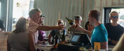 A server pours wine for a customer at a tasting counter inside a building.