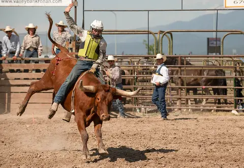 A cowboy rides a bucking bull in an arena.