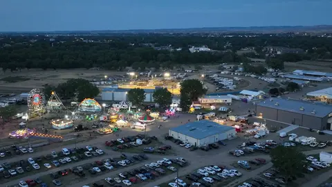 An aerial view shows a fairgrounds lit up at dusk with rides and parking lots filled with vehicles.