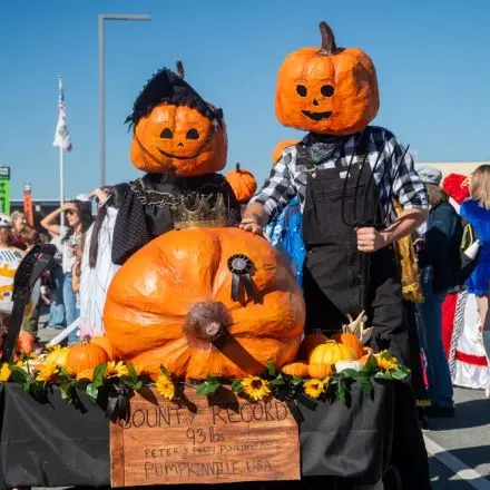 People in pumpkin masks and costumes participate in an outdoor event.