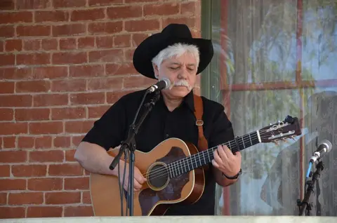 A man wearing a cowboy hat plays an acoustic guitar and sings into a microphone.
