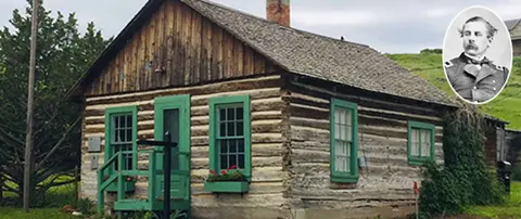 A historic log cabin with green trim and an inset portrait of a man in uniform.