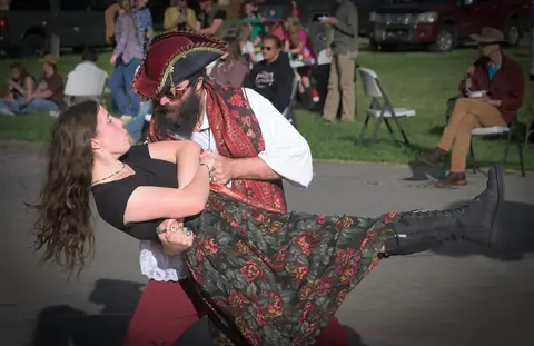 A man dressed as a pirate dips a woman while dancing outdoors.
