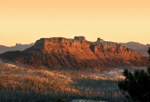 A mountain ridge rises above a forested valley at sunset.