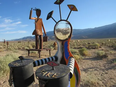 A colorful sculpture with a give and take box stands in a desert landscape.