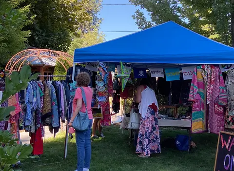 A person browses clothing at an outdoor market stall under a blue canopy.