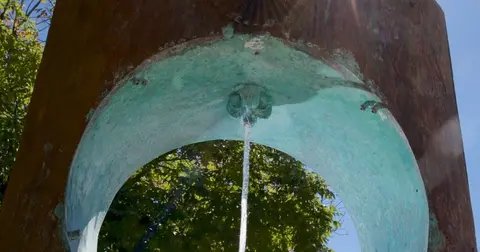 Water streams from an ornate fountain with a weathered, patina-covered arch.