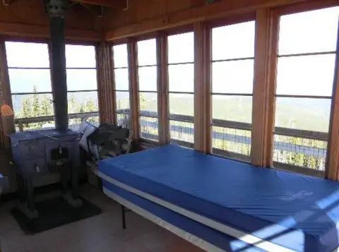 The interior of a wooden cabin with large windows and a stove.