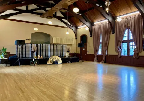 A large wooden hall with a stage, polished floors, and exposed ceiling beams.
