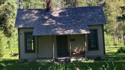 Exterior view of a small historic wooden cabin with a shingled roof and front porch.