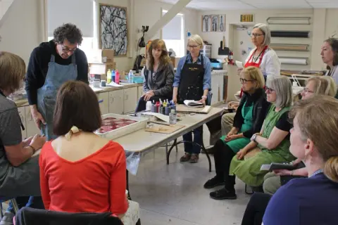An art instructor demonstrating a technique to a group of attentive students in a studio.