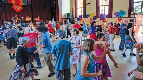A large group of people dancing together inside a hall.