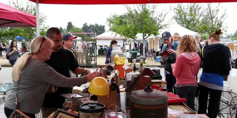 People browse items at an outdoor flea market booth.