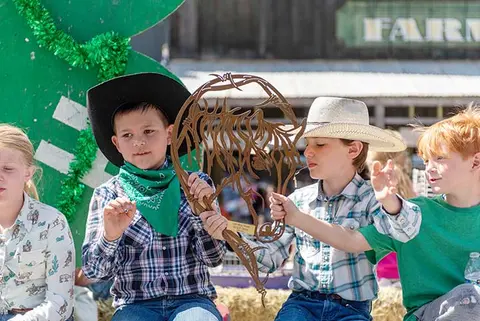 Children in cowboy hats hold a metal art piece outdoors.