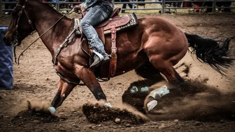 A rider on a horse making a sharp turn in a dirt arena.