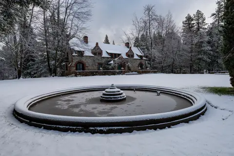 A stone house and round fountain covered in snow.