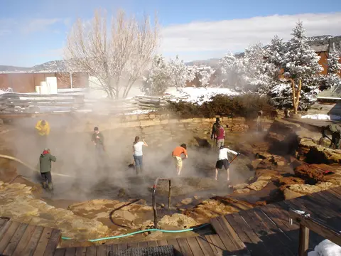 People working inside a steaming outdoor hot spring pool surrounded by snow.